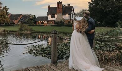 Image shows a bride and groom, at dusk, looking over the lake at the farm house on their big day