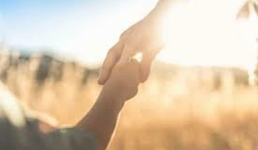 An image of a young boy holding his mum's hand, as they walk through a field of wheat on a sunny day