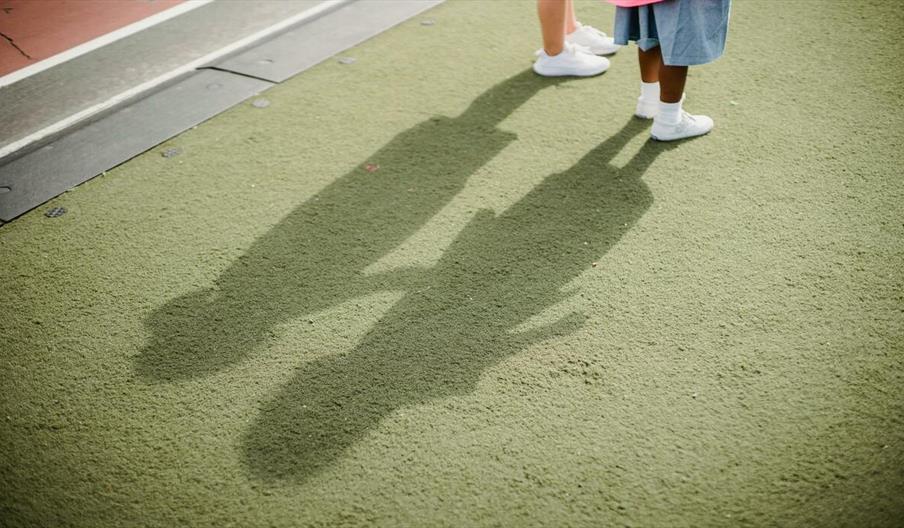 Two children casting shadows on a green surface