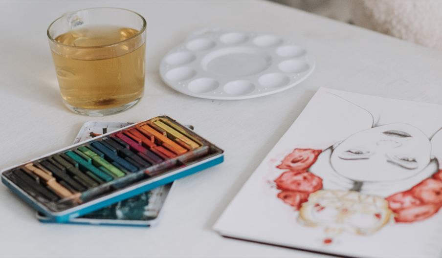 A set of oils and a sketch of a woman wearing flowers on a white table