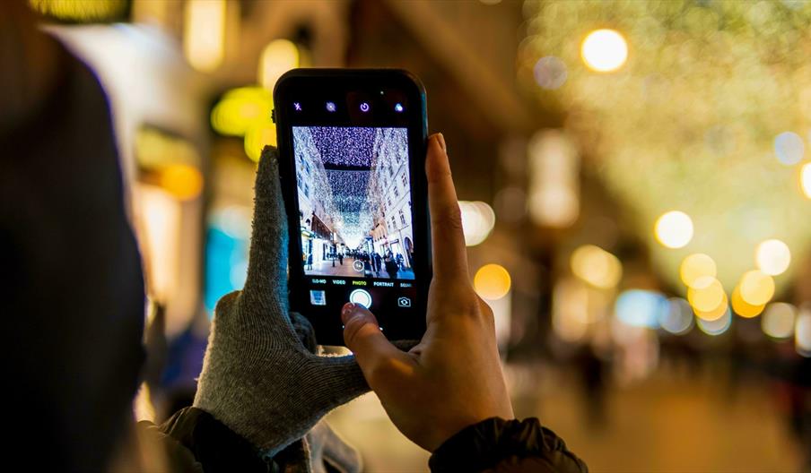Person with one glove off taking a photo of a Christmas street light display