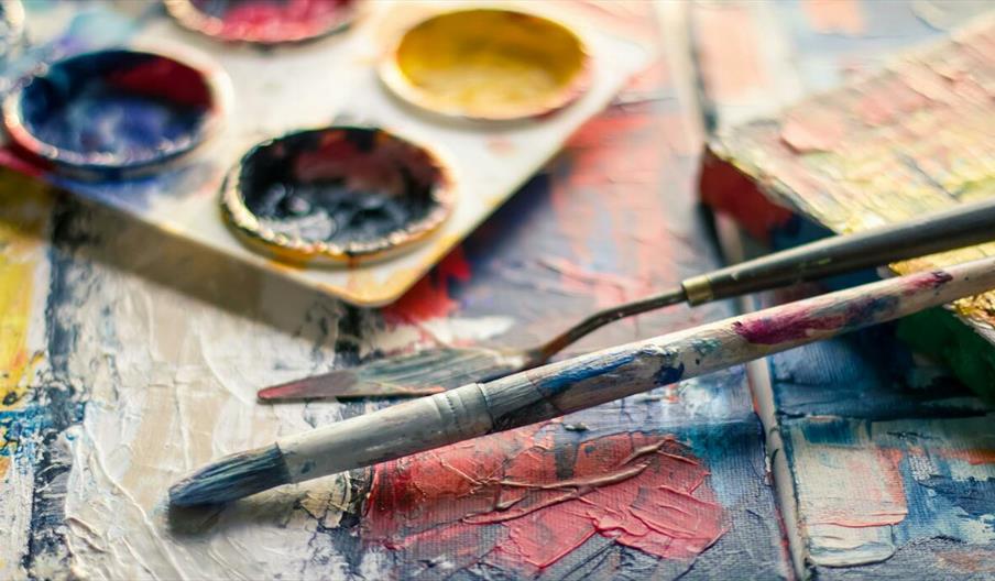 Close-up of colourful paintbrushes and artist palette on a textured canvas