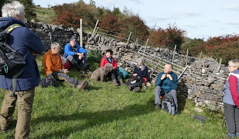 A GROUP OF WALKERS TAKING A REST BY A STONE WALL