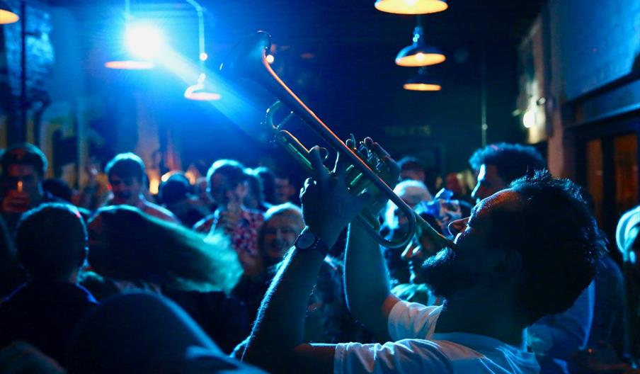 A man plays a trumpet in a crowded venue, possibly a nightclub
