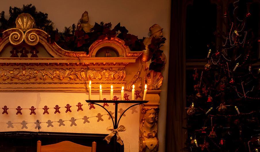 Candles on a candelabra beside a Christmassy-looking fireplace