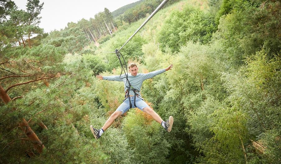A man flies through the air on a zip wire, going straight through the treetops in a forest
