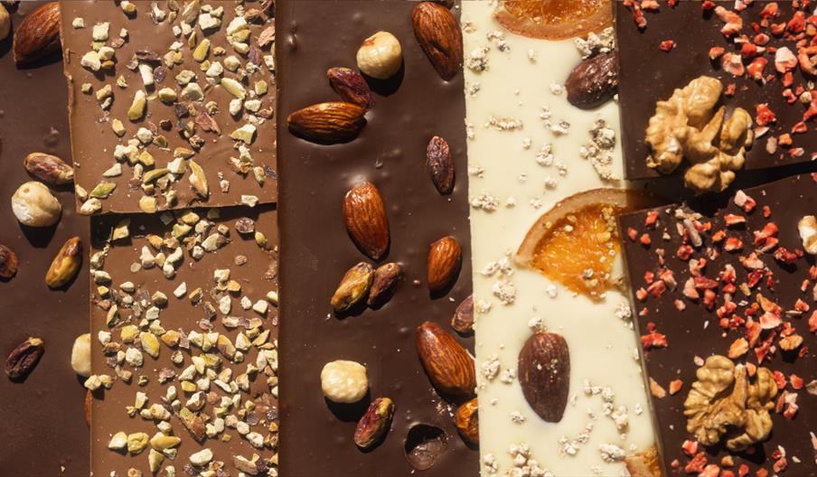 Close-up of assorted artisan chocolate bars topped with nuts, pistachios, dried fruit and candied orange slices.