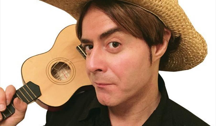 A white male, wearing a cowboy hat and holding a small guitar