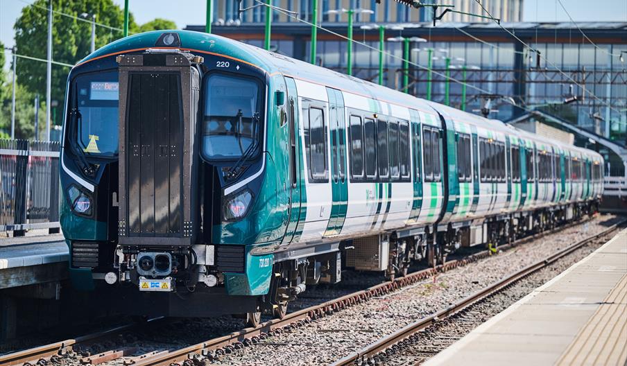 A new train, with London North Western livery, beside the platform in a station, on a sunny day.