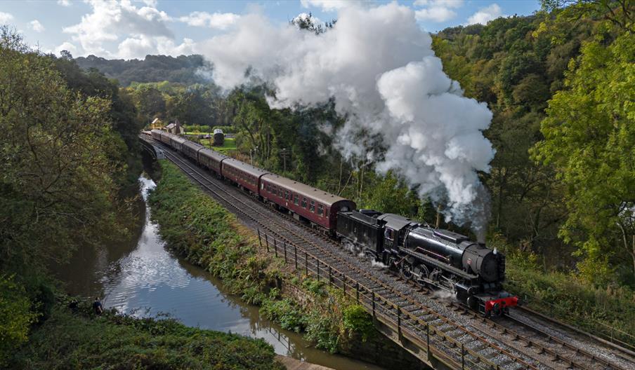 ariel image of a steam train running along it tracks beside the river