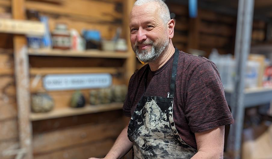 An image of Dave Short, looking at the camera, wearing a clay-covered apron