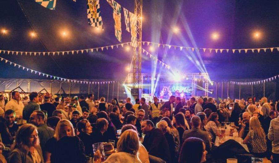 photo depicts an oktoberfest scene of long tables with people eating and drinking at night time