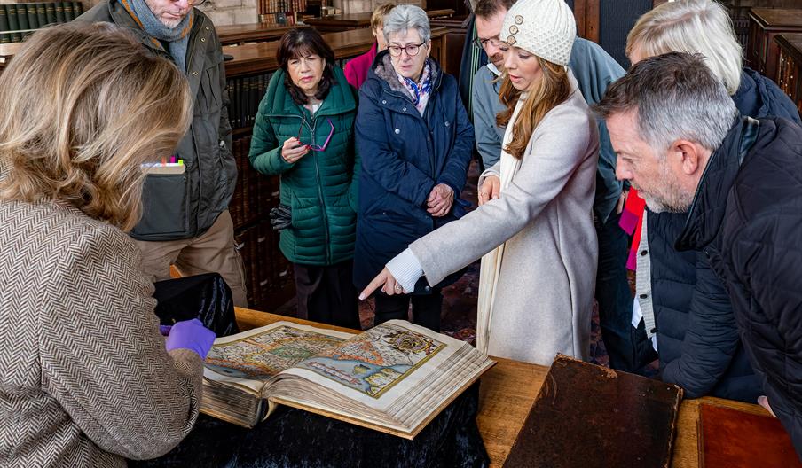 Image shows a crowd of people around an old book, with someone pointing at one of the pages