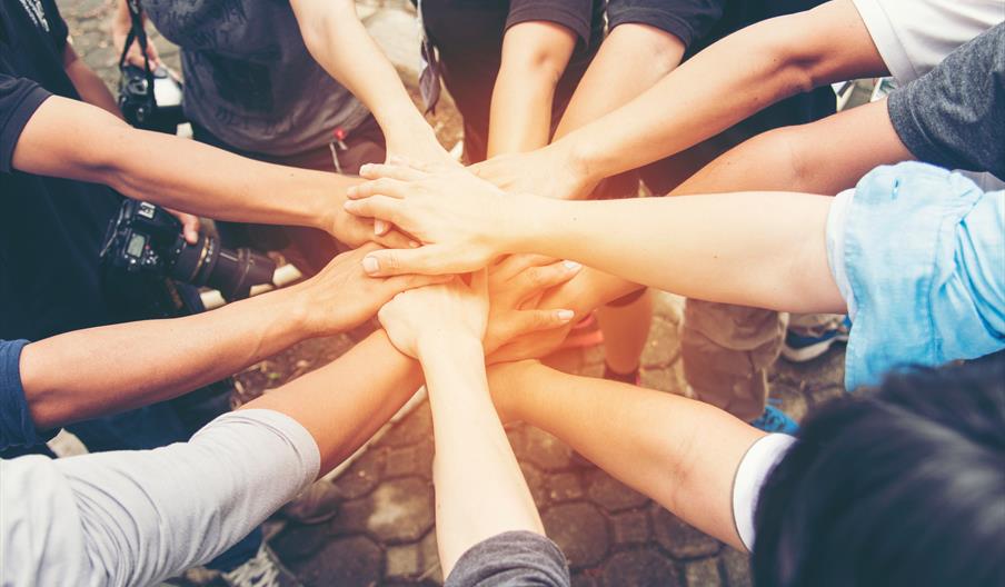 Image shows people in a circle with their hands on top of each other