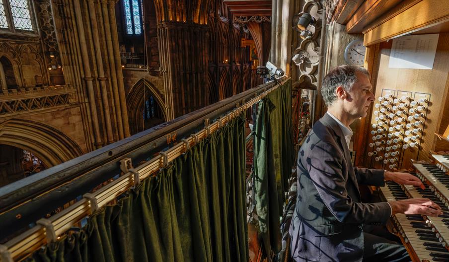 Image shows a man, on the right, playing the organ in a historic building, Lichfield Cathedral