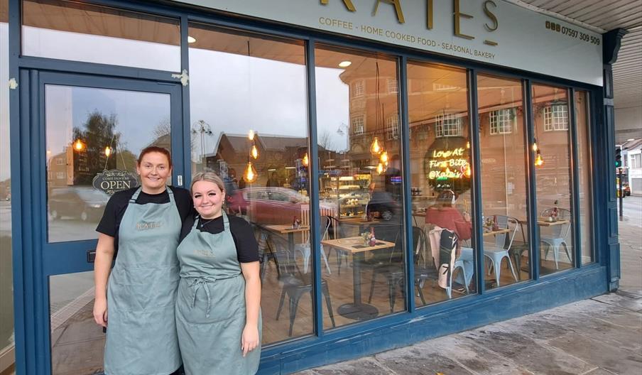 Image shows two women in aprons standing outside a cafe, with KATE'S in big letters above them