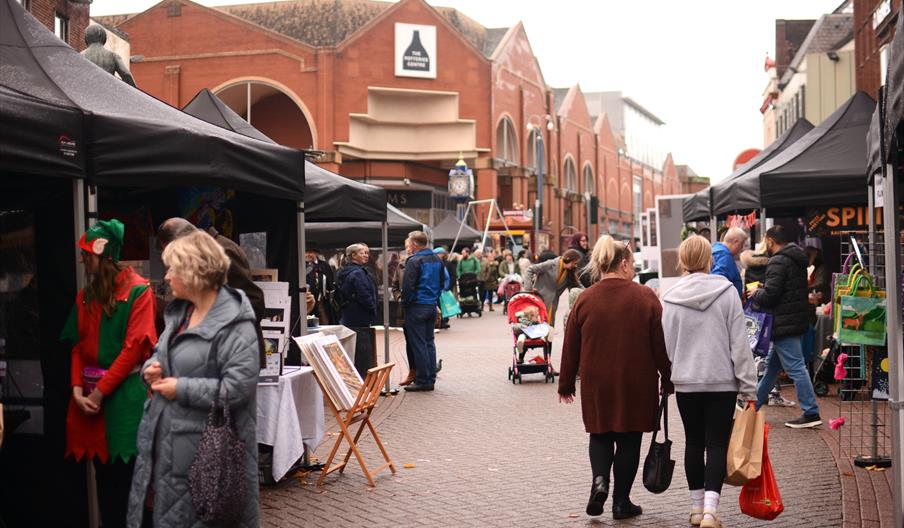 Image shows stalls and shoppers at the Potteries Artisan Market on a grey day