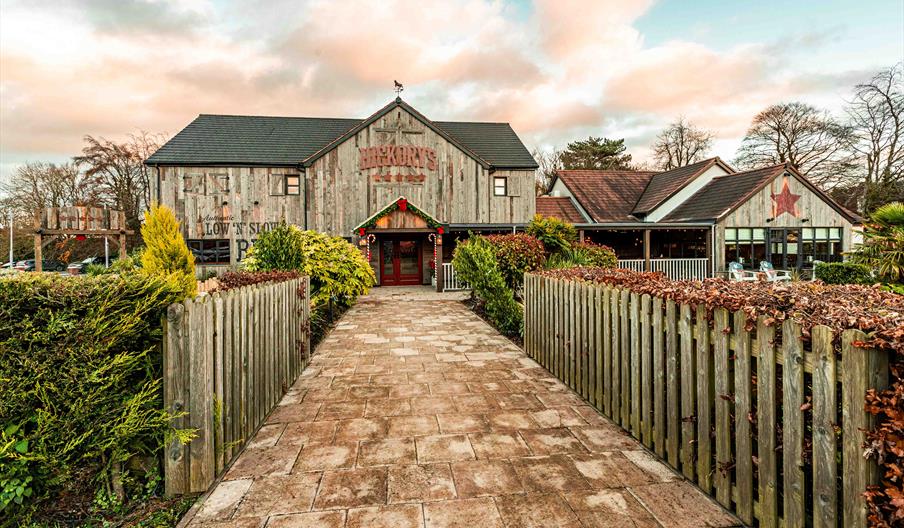 Image shows the approach to Hickory's, with picket fences on both sides and well maintained hedges