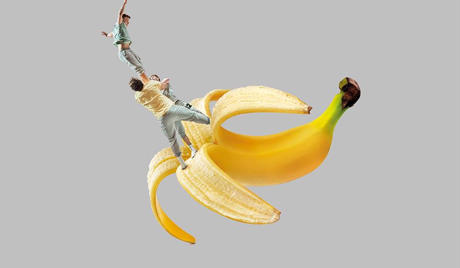Image shows three performers standing on a huge banana skin