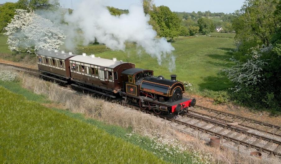 Image shows a heritage steam train chugging through green countryside