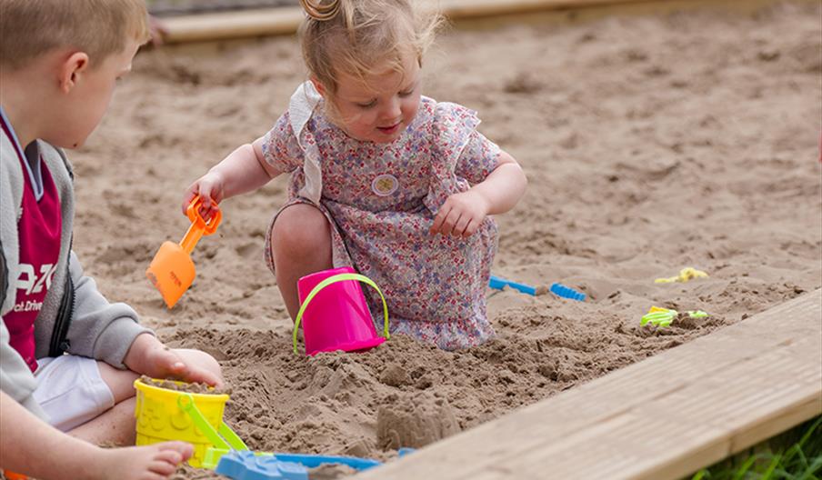 two children playing in a sand pit with brightly coloured buckets and spades