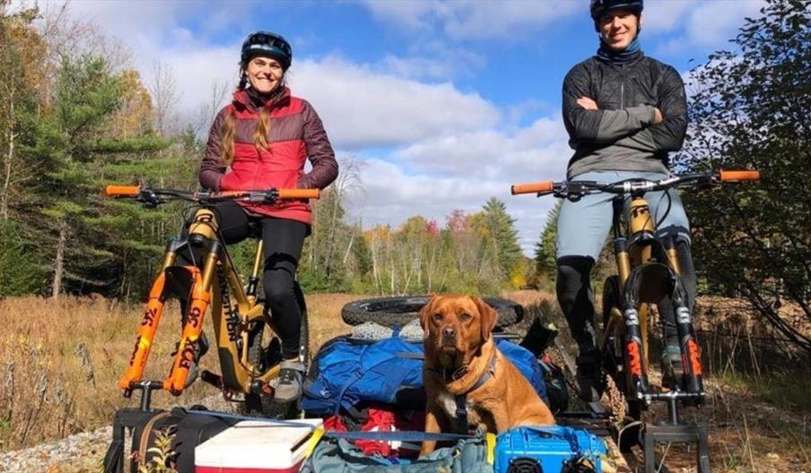 image of female and male cyclist with a dog  and camping equipment