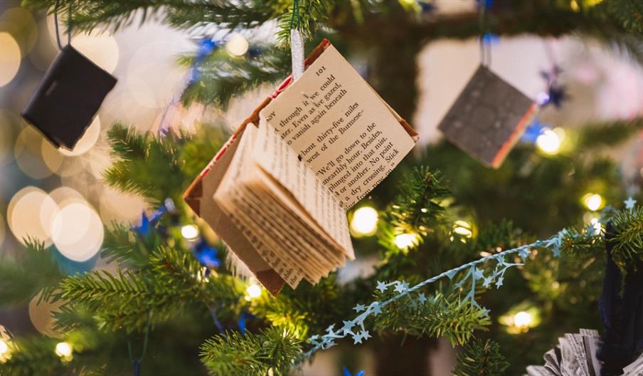Image shows a book decoration hanging from the branch of a Christmas tree