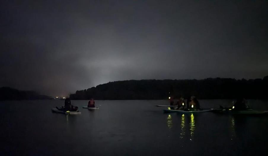 image of paddle boarders at nigh time with headlights