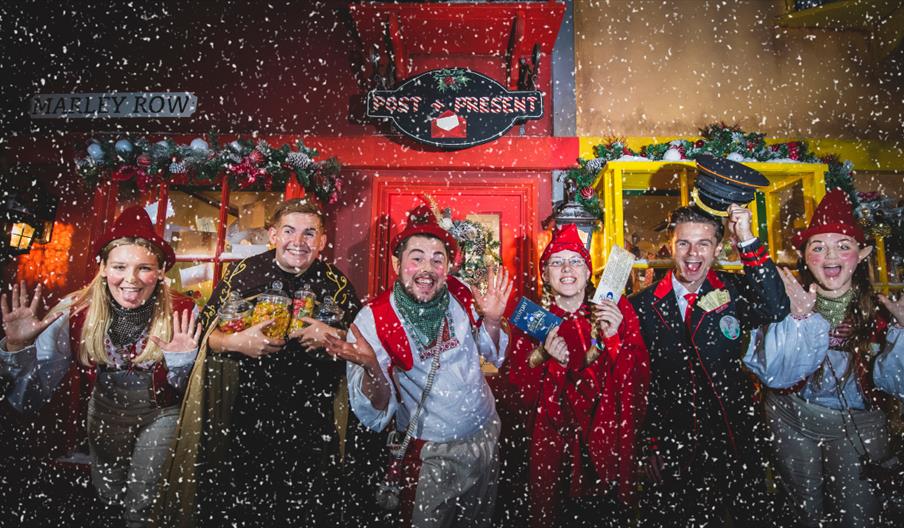 Image shows some of the performers from North Pole Adventure, in costumes, as snow falls down
