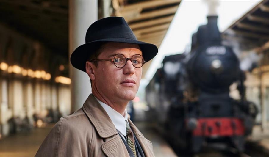 image of a man standing at a railway station with a steam train the the background