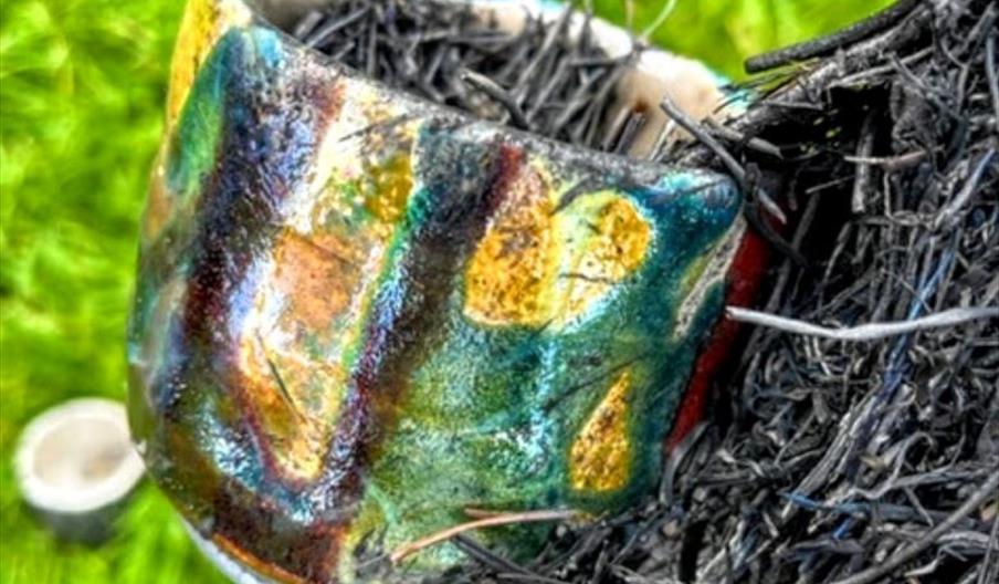 Colourful glazed pot filled with dark fibres in a garden setting.