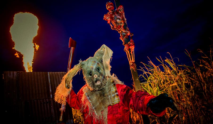 Image shows a frightening character from Screamfest, with fire shooting up into the night sky in the background