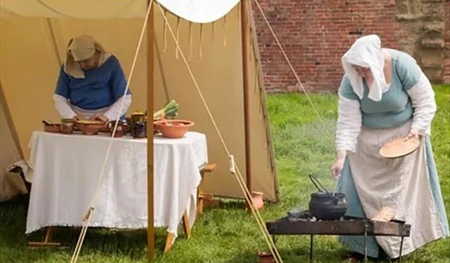A demonstration of medieval life, with two women making food - one cooking using a pot on an open fire and the other preparing vegetables