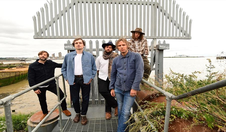 Image shows a group of men standing at the top of a metal staircase by the sea
