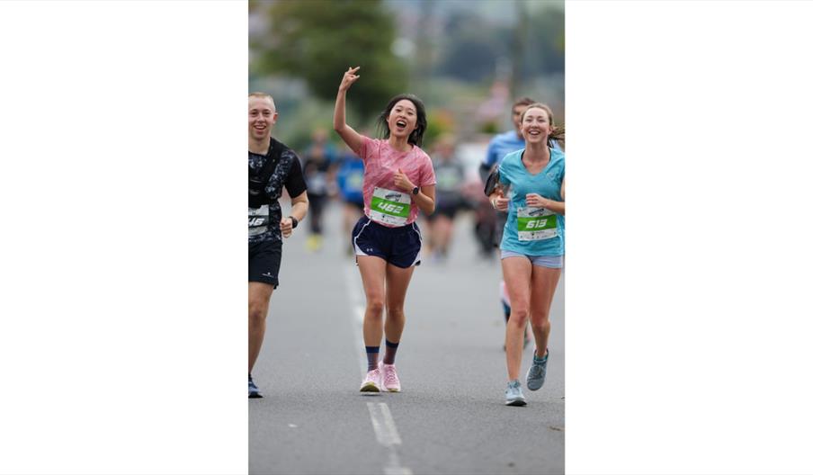 Runners crossing a city centre finish line, raising arms in celebration during a road race event.