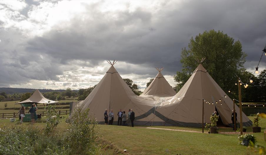 Large beige outdoor tent like structure, surrounded by trees and string lights.