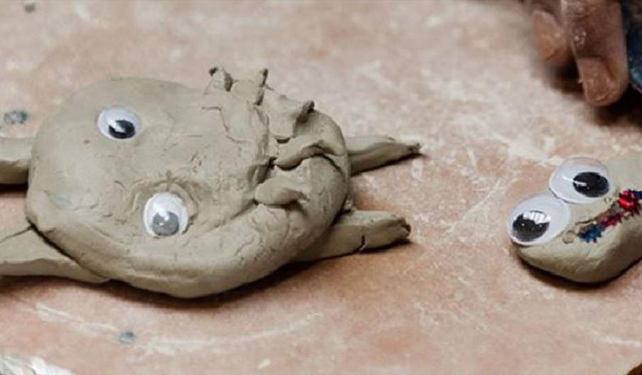 Two small clay creatures made from air‑dry clay, decorated with googly eyes and simple sculpted details, placed on a work surface.
