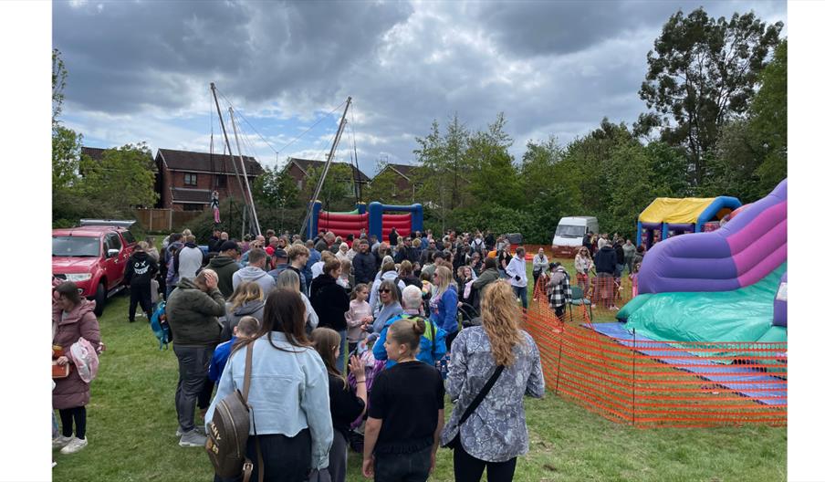 Crowds enjoying a colourful outdoor community fun day with bouncy castles and inflatables.