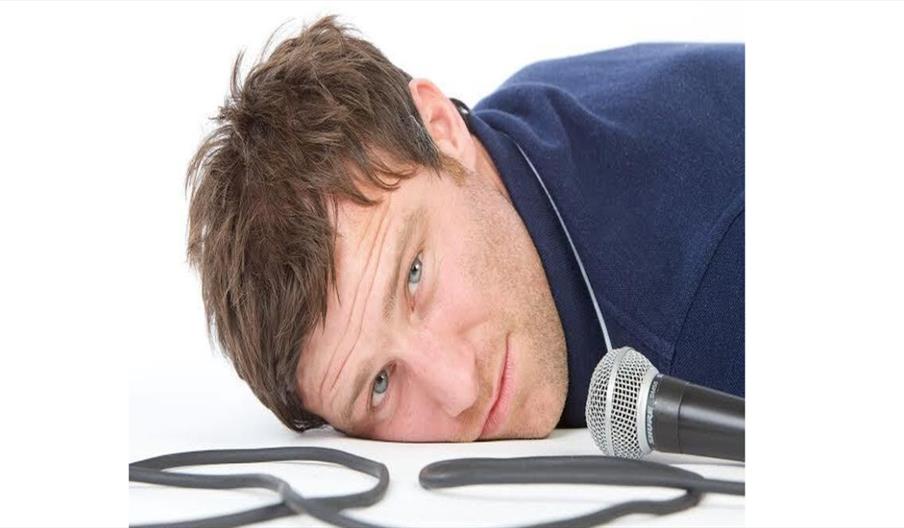 Comedian lying next to a microphone, ready for a night of stand‑up comedy.