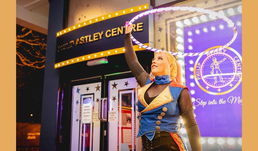 A woman in circus costume spins a hula hoop in front of the Philip Astley Centre in Newcastle-under-Lyme.