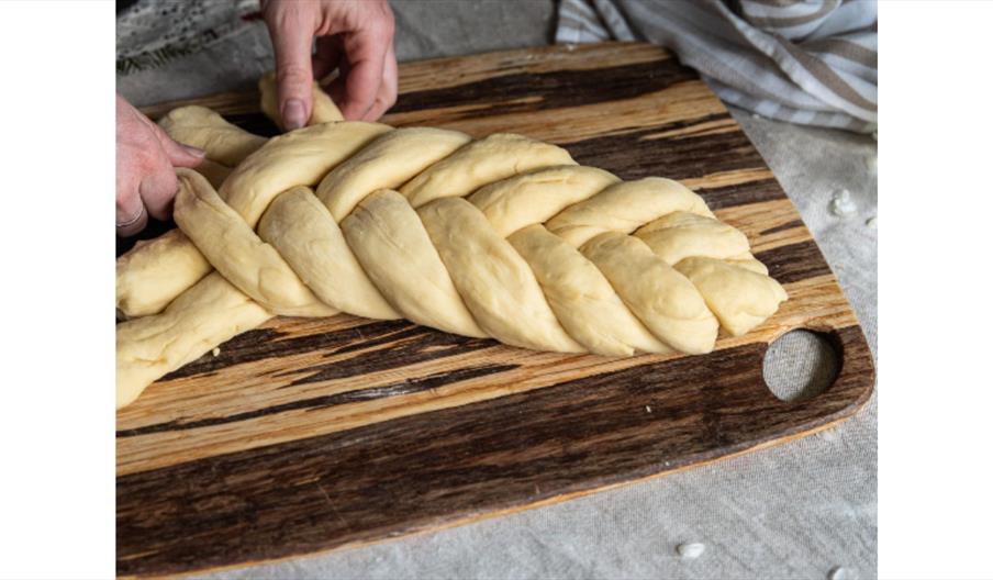 Plaited bread dough being shaped on a wooden board.