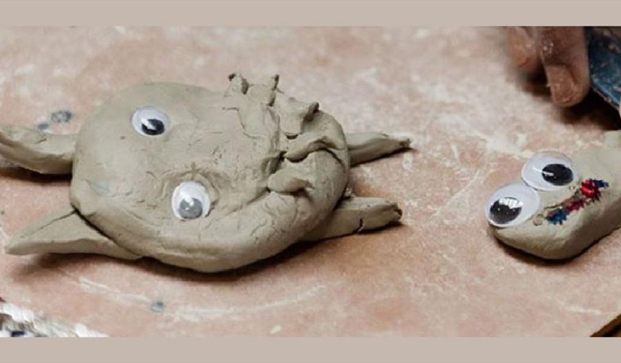 Two small clay creations with googly eyes placed on a work surface. One of them is decorated with colourful details.