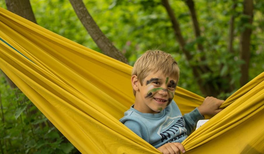 A boy, with his face covered in war paint, tries out a hammock