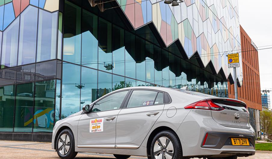 A gleaming grey/silver taxi parked outside a colourful building