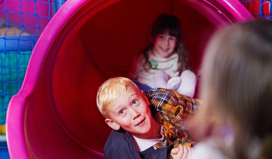 Image shows a young boy at the bottom of a slide in a children's indoor play area
