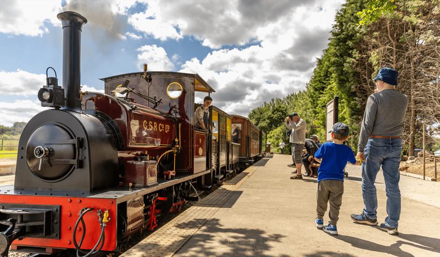 A father and son about to board a heritage steam train on a sunny day
