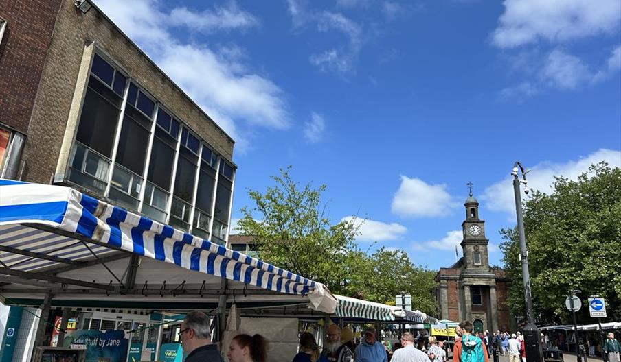 A glorious sunny day, with people visiting market stalls and a historic clock tower in the background