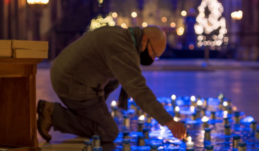 Image shows a man lighting candles on the floor of an old building