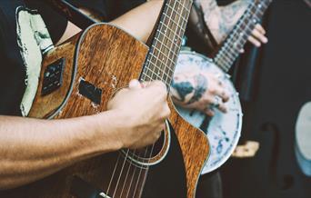 Person playing a banjo and another playing a dark wood acoustic guitar and another with a double bass