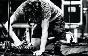 Black and white image of a person plugging in a pedalboard on stage